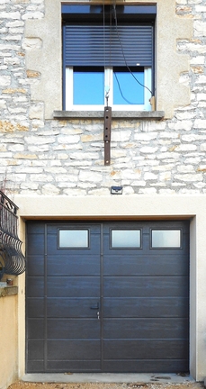 Porte sectionnelle (refoulement par le haut) équipé d'un portillon piéton et vitrages pour créer des entrées de lumière dans le garage.